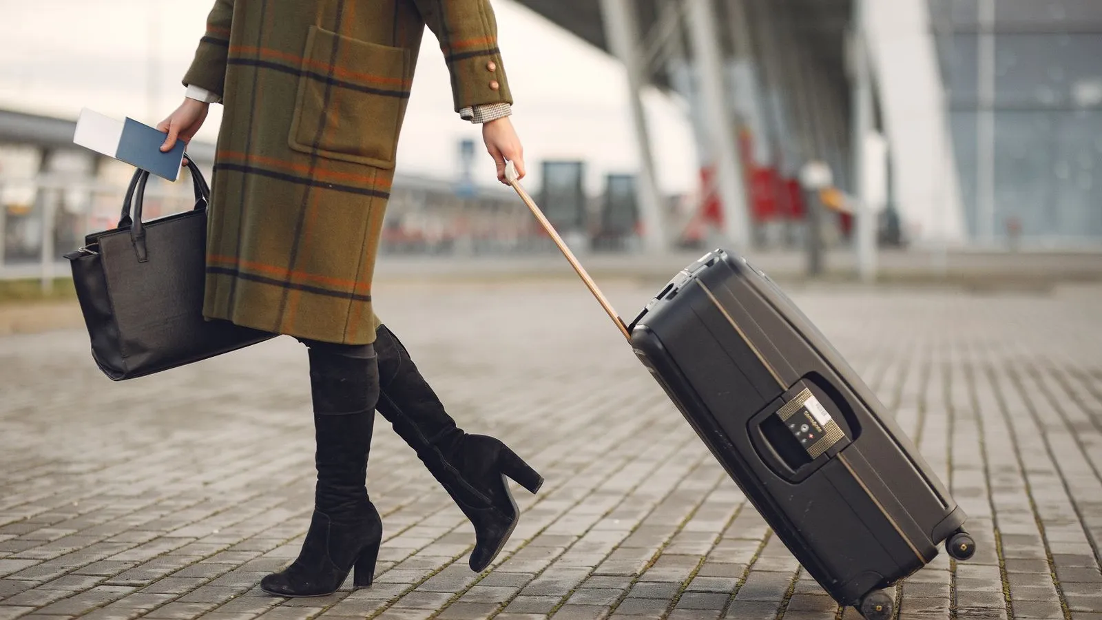 Viajante com passaporte na mão a puxar uma mala de rodas à saída de um terminal de aeroporto.