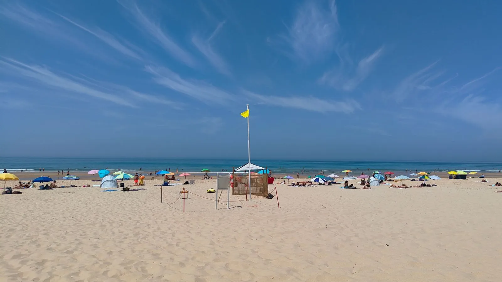 Praia da Costa da Caparica num dia de sol, com chapéus de sol coloridos junto ao mar.