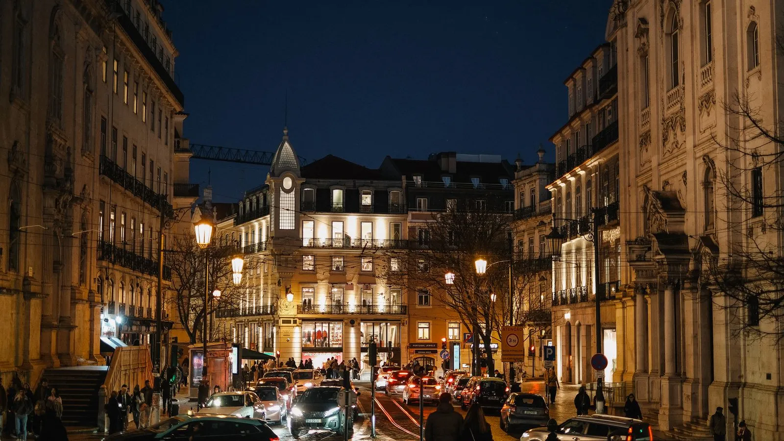 Rua do Chiado à noite, em Lisboa, com candeeiros acesos e pessoas a caminho do Bairro Alto.