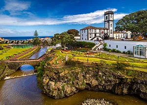 Jardim e ponte de pedra sobre uma ribeira, com o mar ao fundo